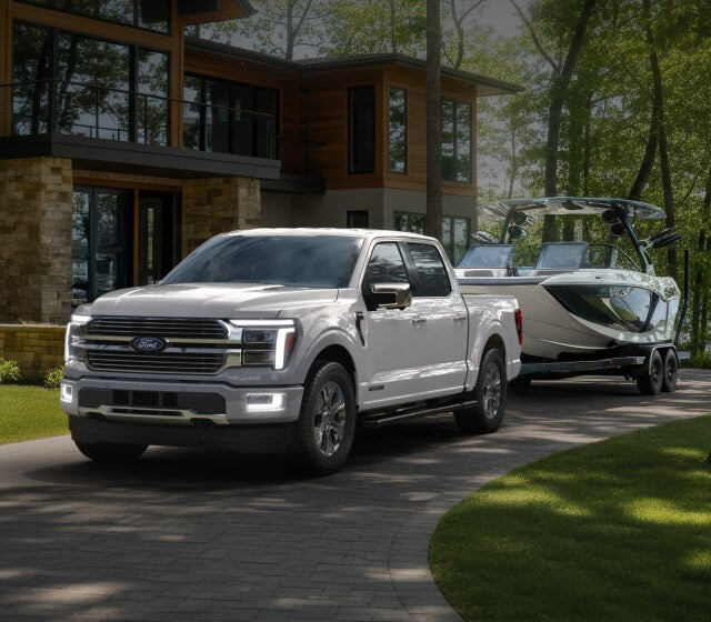 A light silver Ford F-150 parked in an upscale driveway while towing a boat.