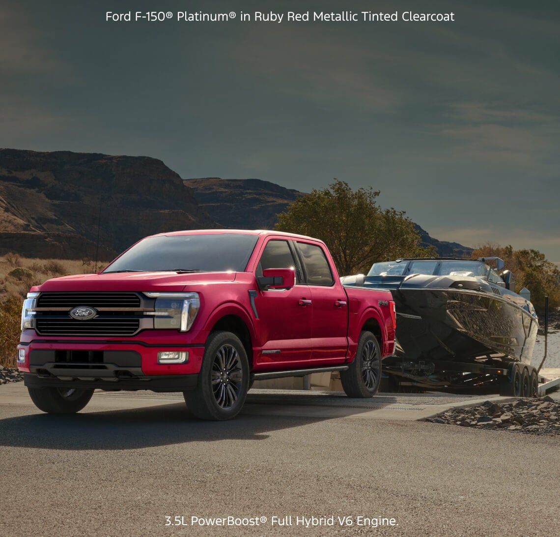 Front quarter view of a Ford F-150 Platinum in Ruby Red Metallic towing a motorboat up a concrete boat ramp.